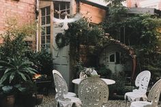 there are many white chairs and tables in the yard with flowers on them, near an old brick building