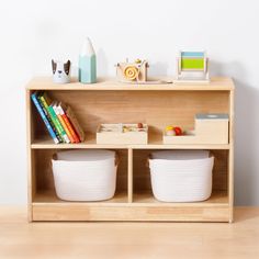 a wooden shelf with two white baskets on top of it next to books and toys