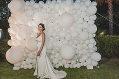 a woman standing in front of a giant bunch of white balloons on the grass at night