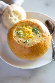 a white plate topped with a bowl of broccoli soup next to two rolls