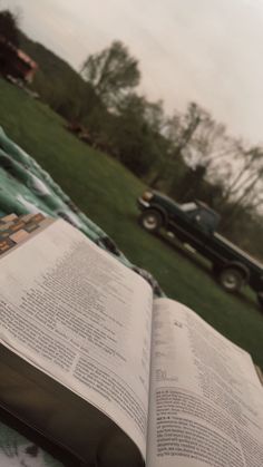 an open book sitting on top of a blanket in front of a green field with a truck