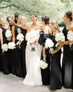 a group of women standing next to each other wearing black dresses and holding bouquets