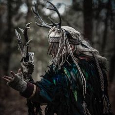 a man dressed in native american clothing with horns and feathers on his head, holding an animal's antlers