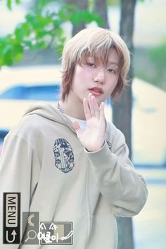 the young man is wearing a hoodie and making a hand gesture while standing in front of a tree