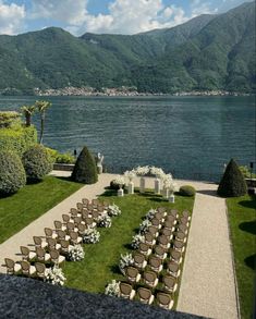 an outdoor ceremony set up with chairs and flowers on the lawn by the water in front of mountains