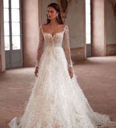 a woman in a white wedding dress with long sleeves and feathers on the skirt is standing in an empty room