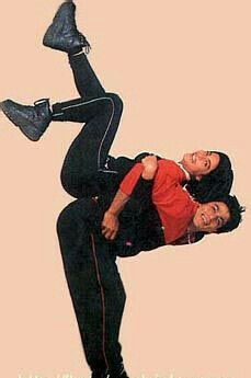 two people in black pants and red shirt doing a trick on one another with their feet up