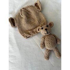 a crocheted teddy bear laying next to a knitted hat on a white sheet