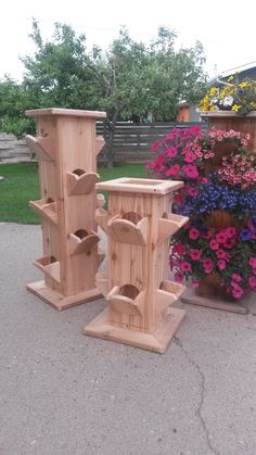 two wooden bird feeders sitting next to each other in front of flowers and potted plants