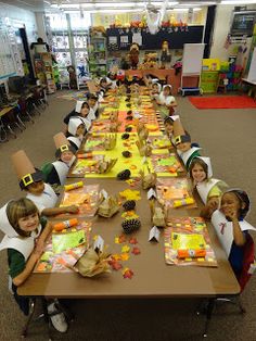 a group of children sitting at a long table with paper hats on their heads and hands