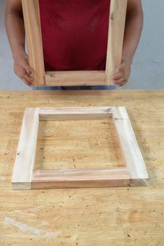 a person standing over a wooden table with a square frame on it's side