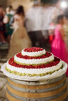 a wedding cake sitting on top of a wooden barrel next to people in the background