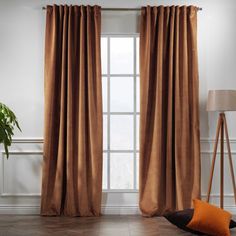 a living room with a large window covered in brown curtains and two orange pillows on the floor