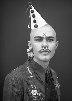 a black and white photo of a man wearing a party hat with nose piercings