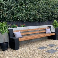 a wooden bench sitting in the middle of a gravel covered area with potted plants