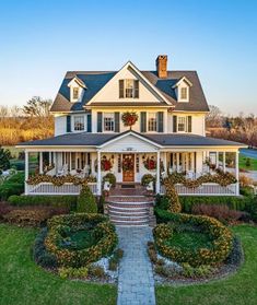 a large white house with wreaths and flowers on the front porch, surrounded by greenery