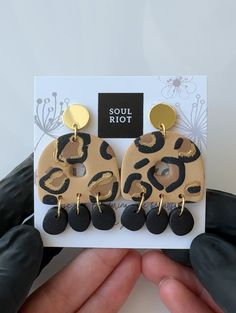 a pair of leopard print earrings on top of a white card with black and gold accents