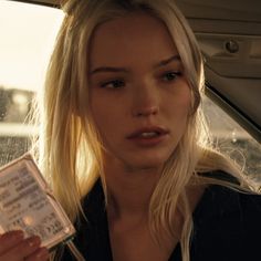 a blonde woman sitting in the back seat of a car holding a ticket and looking at the camera