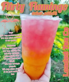 a person holding up a pink and orange drink in front of a green field with trees