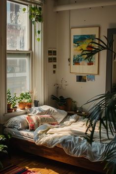 an unmade bed sitting in front of a window next to a potted plant