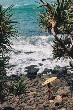 a person holding a surfboard on top of a rocky beach next to the ocean