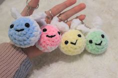 four small crocheted keychains with faces on them are being held by someone's hand