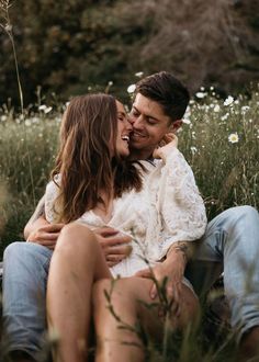 a man and woman are sitting in the grass with their heads close to each other