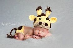 a baby wearing a crocheted giraffe hat laying on top of a blanket