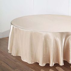 a round table with a white cloth on it in front of a wall and wooden floor