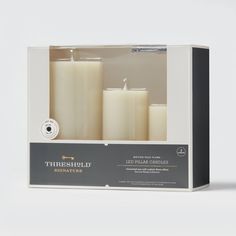 three white candles in a box with the packaging on it's front and side