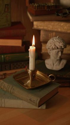 a lit candle sitting on top of a book next to a busturine and stack of books