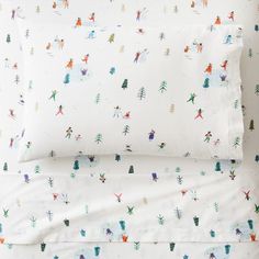 a bed with white sheets and colorful christmas trees on the sheet set, along with two pillow cases