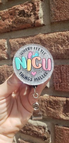 someone holding up a badge with the word nicu on it in front of a brick wall