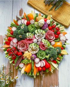 an arrangement of vegetables arranged in a circular arrangement on a wooden surface with flowers and herbs