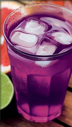 a purple drink with ice and limes on the side