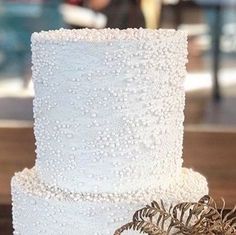 a three tiered white wedding cake decorated with pearls