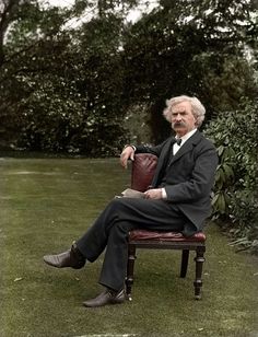 an old photo of a man sitting on a chair in the grass with trees behind him