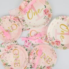 pink and gold floral plates with the word one on them are laid out next to each other