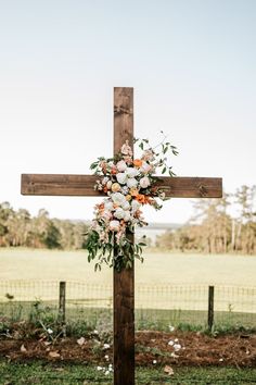 a cross decorated with flowers and greenery for a wedding ceremony in the country side