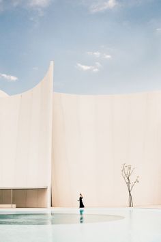 a person standing in front of a large building with a tree next to the pool