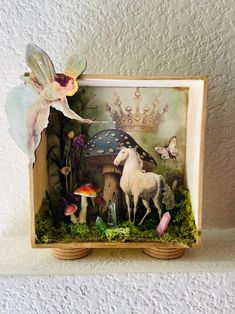 a miniature fairy scene with a unicorn, mushroom, and mushrooms in a wooden frame