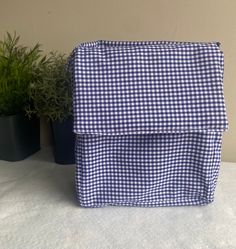 a blue and white checkered backpack sitting on top of a table next to potted plants