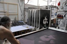 a woman working on an art piece in a studio with lots of artwork behind her