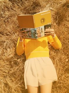 a woman laying on the ground reading a book in front of her face and head