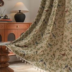 a curtain with birds on it is hanging in front of a dresser and table lamp