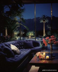 a living room filled with furniture next to tall windows at night and lit candles on the coffee table