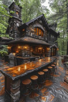 an outdoor bar with lots of stools in front of a stone building surrounded by trees