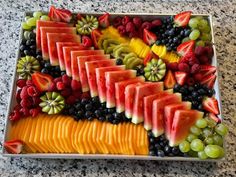 a tray filled with sliced up fruit on top of a marble countertop next to grapes, kiwis and watermelon