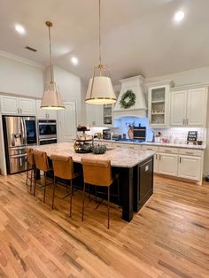 a large kitchen with white cabinets and wooden flooring, along with an island in the middle