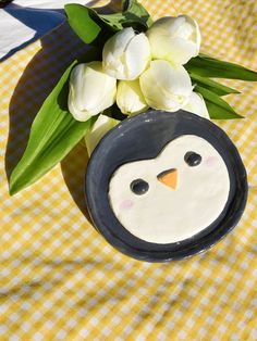 a penguin vase with tulips in it on a yellow and white checkered table cloth